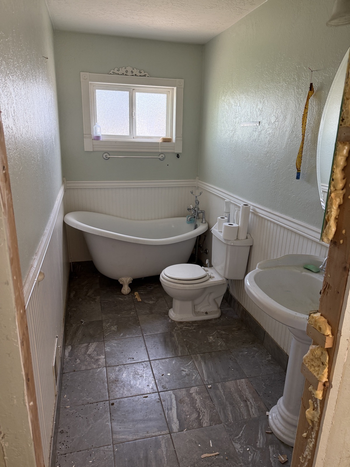 Dated bathroom with a clawfoot tub, mint walls over white beadboard, dark tile floor and the door casing stripped back to bare wood